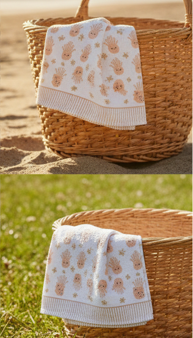 Baby blanket with teddy bear pattern in a wicker basket on sand and grass