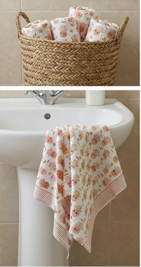 Set of towels with a floral pattern on a wooden table, in a basket, and hanging on a towel rack.