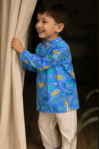 Child wearing a blue shirt with fish pattern and white pants, standing behind a curtain.