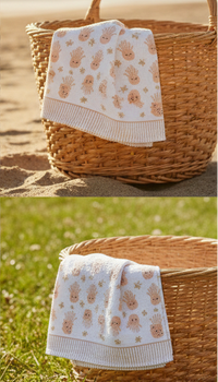 Baby blanket with teddy bear pattern in a wicker basket on sand and grass
