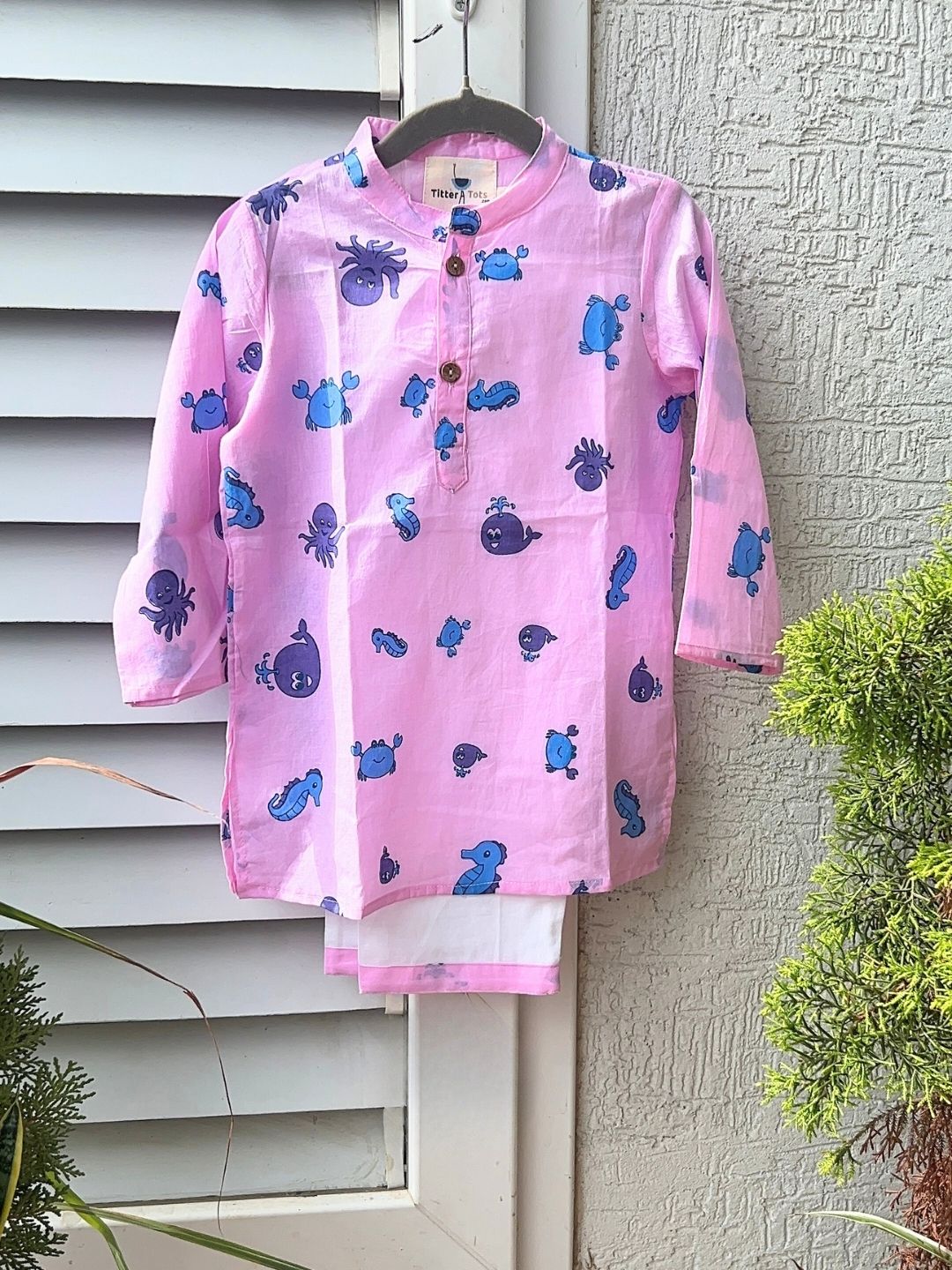Pink shirt with blue whale patterns hanging on a white wall